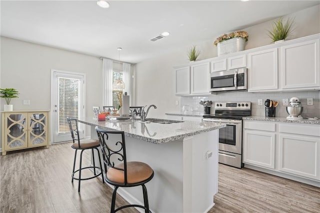 kitchen with sink, white cabinetry, tasteful backsplash, appliances with stainless steel finishes, and a kitchen island with sink