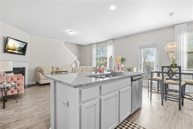 kitchen featuring sink, light wood-type flooring, dishwasher, an island with sink, and pendant lighting