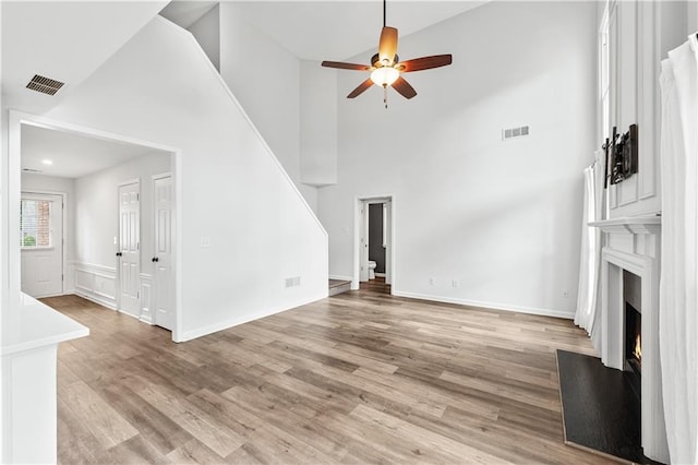 615 Rosedown Way, Alpharetta, GA 30022 - unfurnished living room featuring ceiling fan, a high ceiling, a warm lit fireplace, light wood-style floors, and stairs