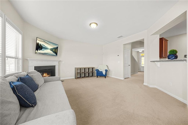living area featuring light carpet, a glass covered fireplace, and baseboards