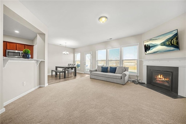 carpeted living room with an inviting chandelier, a fireplace with flush hearth, and baseboards