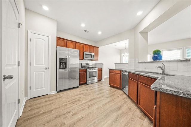 kitchen with a sink, visible vents, appliances with stainless steel finishes, light wood-type flooring, and dark stone countertops