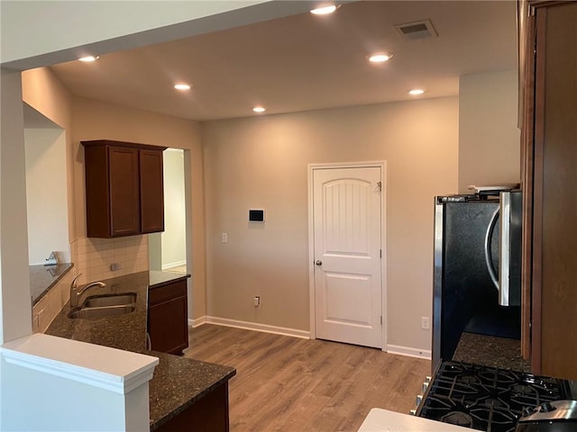 kitchen featuring stainless steel refrigerator, sink, dark stone counters, decorative backsplash, and light wood-type flooring