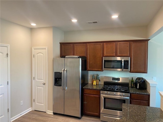 kitchen with appliances with stainless steel finishes, backsplash, light hardwood / wood-style floors, and dark stone counters