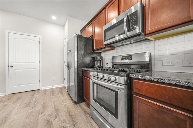 kitchen featuring stainless steel appliances, baseboards, decorative backsplash, light wood finished floors, and dark stone countertops