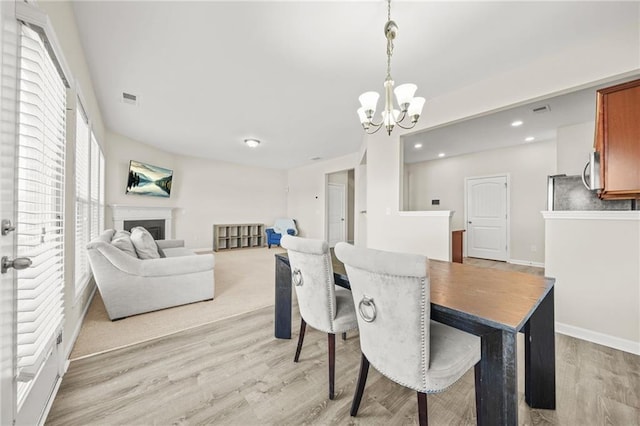 dining space with light wood-style flooring, a fireplace, visible vents, and a notable chandelier