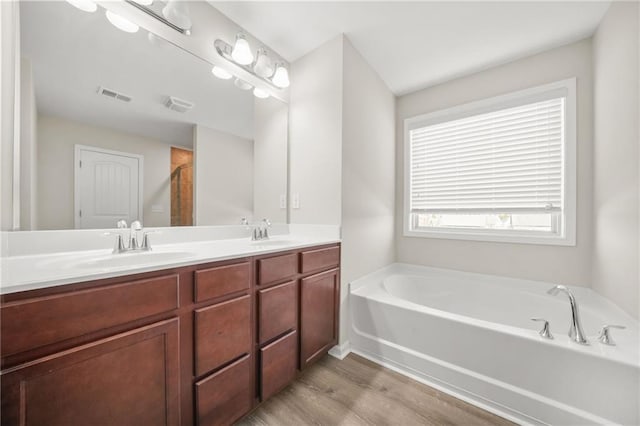 full bath featuring a garden tub, visible vents, a sink, and wood finished floors