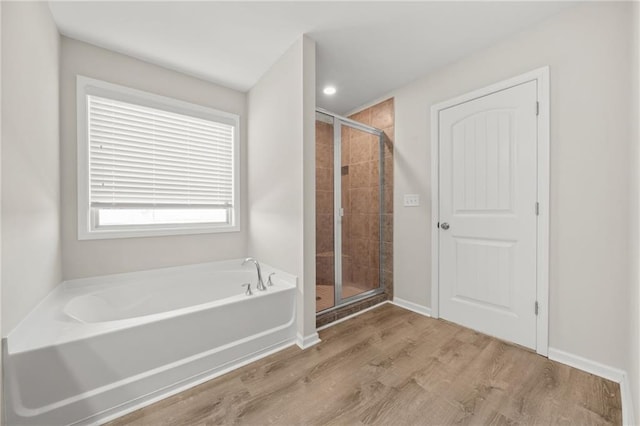 bathroom with a stall shower, baseboards, a bath, and wood finished floors