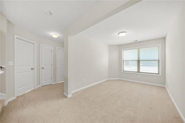 empty room featuring light carpet, visible vents, and baseboards