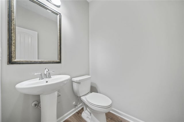 bathroom featuring toilet, a sink, baseboards, and wood finished floors