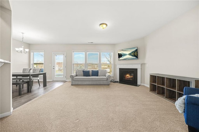 carpeted living area featuring baseboards, a fireplace with flush hearth, and an inviting chandelier