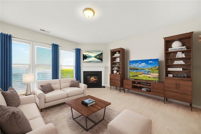 living area featuring a fireplace with flush hearth, light colored carpet, and visible vents