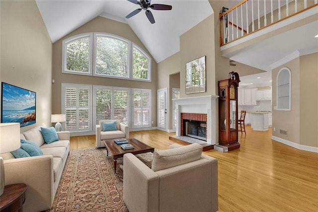 living room featuring ceiling fan, a fireplace, high vaulted ceiling, light wood-style flooring, and visible vents