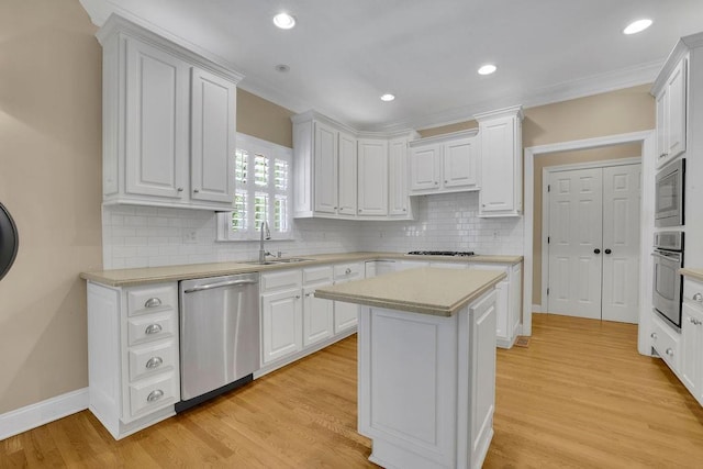 kitchen with a kitchen island, appliances with stainless steel finishes, a sink, light countertops, and white cabinetry