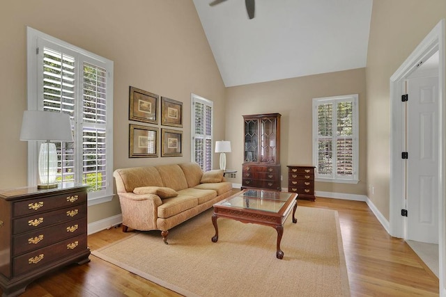 living area with baseboards, ceiling fan, wood finished floors, and high vaulted ceiling