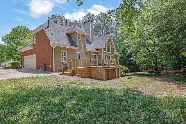 back of property with a wooden deck, a chimney, a shingled roof, concrete driveway, and a yard