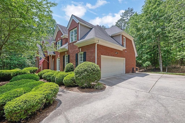 view of side of home featuring brick siding, driveway, a shingled roof, and a garage