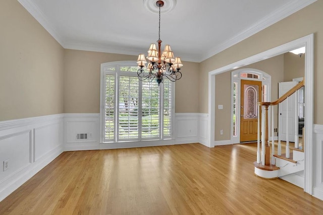 entryway with light wood-type flooring, wainscoting, stairs, and an inviting chandelier