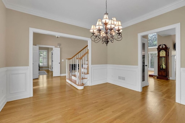 unfurnished dining area with light wood-style flooring, stairs, a notable chandelier, and wainscoting