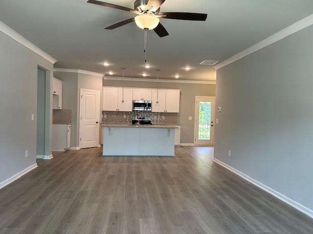 kitchen featuring appliances with stainless steel finishes, dark hardwood / wood-style flooring, white cabinets, a kitchen island with sink, and backsplash