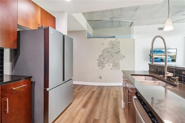 kitchen featuring tasteful backsplash, appliances with stainless steel finishes, light hardwood / wood-style flooring, sink, and decorative light fixtures