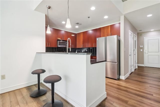 kitchen featuring kitchen peninsula, decorative backsplash, appliances with stainless steel finishes, wood-type flooring, and decorative light fixtures