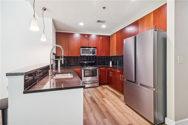 kitchen featuring tasteful backsplash, hanging light fixtures, appliances with stainless steel finishes, light hardwood / wood-style flooring, and sink