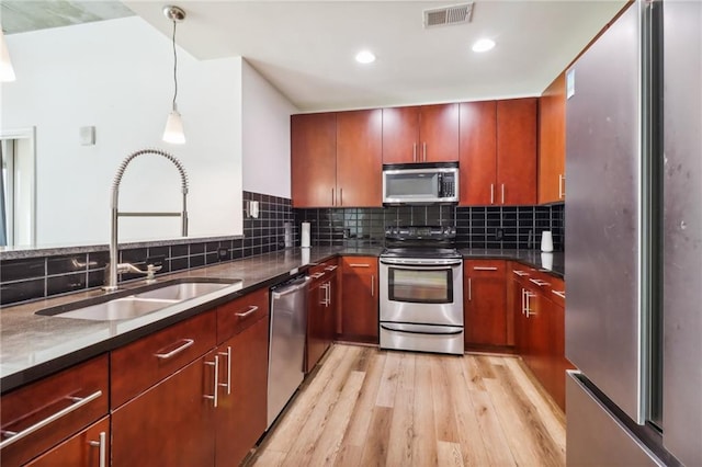 kitchen featuring tasteful backsplash, appliances with stainless steel finishes, sink, light hardwood / wood-style floors, and pendant lighting