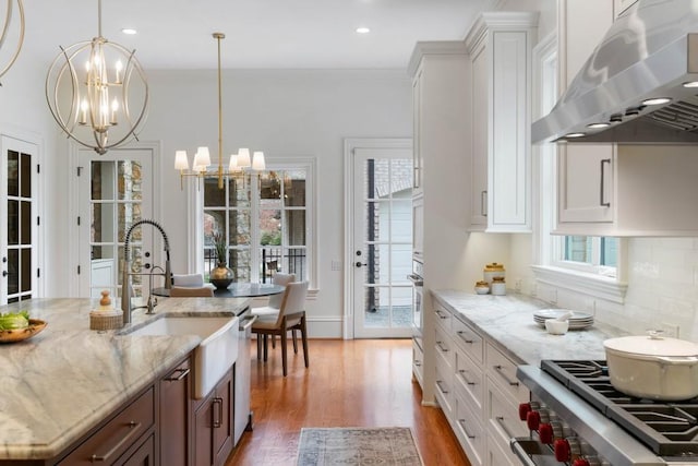 kitchen featuring appliances with stainless steel finishes, pendant lighting, white cabinetry, exhaust hood, and a notable chandelier