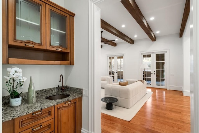 bar featuring sink, light hardwood / wood-style flooring, beam ceiling, light stone countertops, and french doors