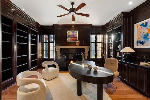 sitting room featuring built in shelves, ceiling fan, wooden walls, and light hardwood / wood-style flooring