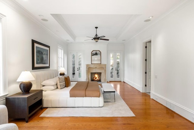 living room with ceiling fan, ornamental molding, light hardwood / wood-style floors, a raised ceiling, and french doors