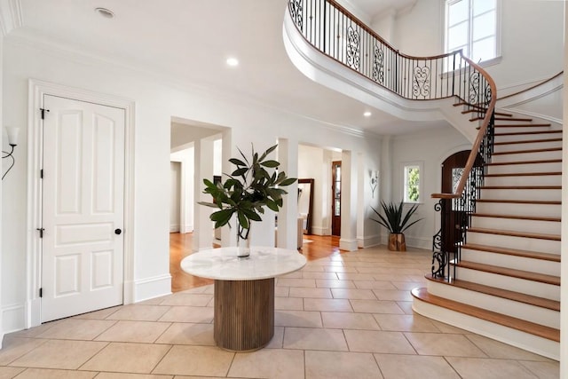 foyer featuring crown molding, a towering ceiling, and light tile patterned floors