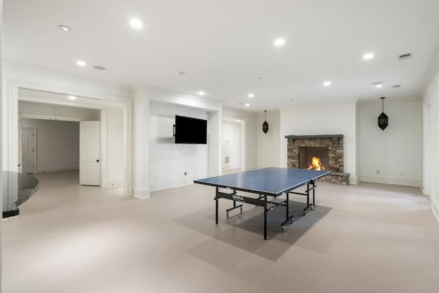 game room with crown molding and a stone fireplace