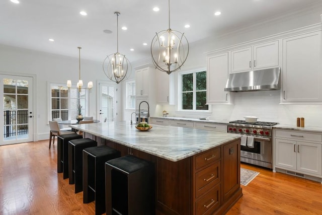 kitchen with white cabinetry, pendant lighting, oven, and an island with sink