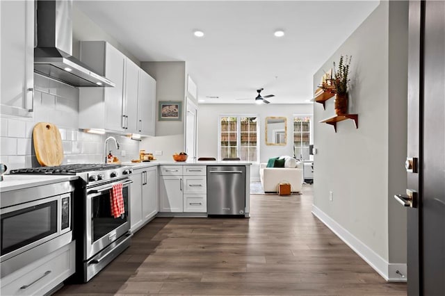 kitchen with dark wood-type flooring, backsplash, stainless steel appliances, white cabinets, and wall chimney exhaust hood