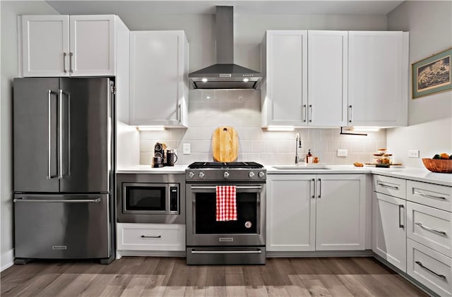 kitchen featuring wall chimney exhaust hood, sink, white cabinetry, appliances with stainless steel finishes, and decorative backsplash