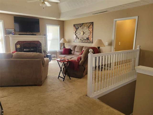 living room featuring a fireplace, light carpet, and ceiling fan