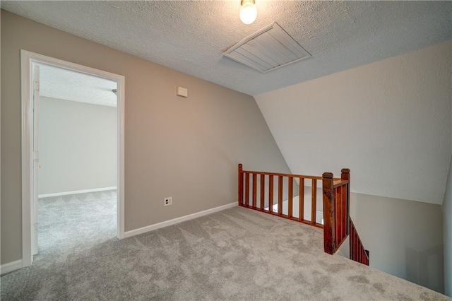 unfurnished room featuring light colored carpet, a textured ceiling, and vaulted ceiling