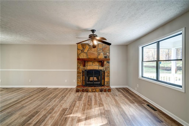 unfurnished living room with a textured ceiling, ceiling fan, hardwood / wood-style floors, and a stone fireplace