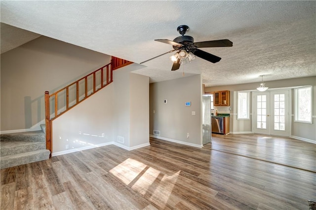 unfurnished living room with ceiling fan, wood-type flooring, a textured ceiling, and french doors