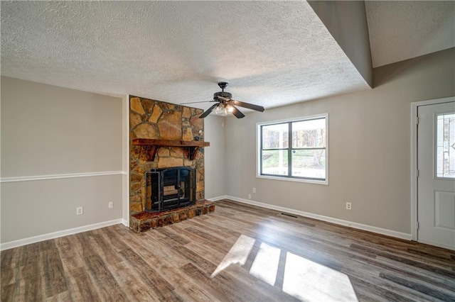 unfurnished living room with a textured ceiling, ceiling fan, hardwood / wood-style flooring, and a stone fireplace