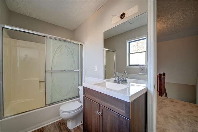 full bathroom featuring combined bath / shower with glass door, vanity, toilet, and a textured ceiling