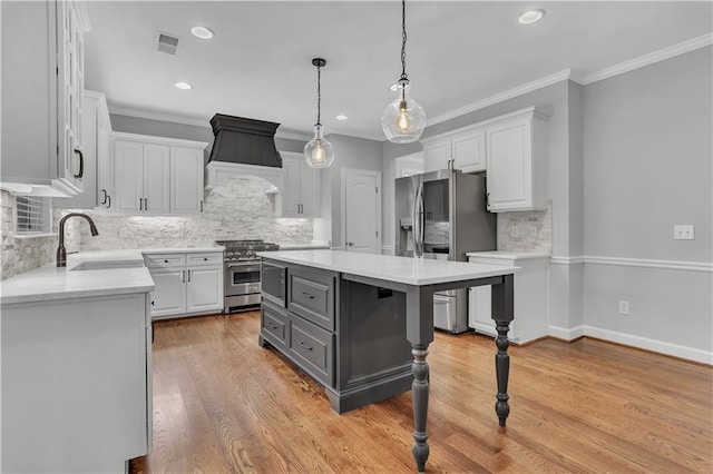 kitchen with appliances with stainless steel finishes, custom range hood, white cabinetry, sink, and a kitchen island