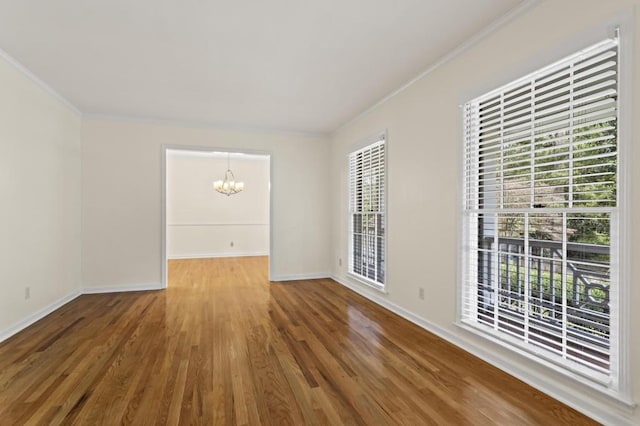 unfurnished room featuring a healthy amount of sunlight, ornamental molding, an inviting chandelier, and hardwood / wood-style floors