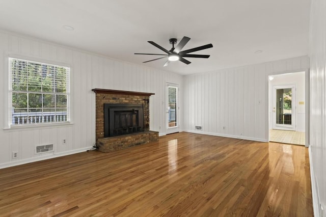 unfurnished living room featuring a healthy amount of sunlight, ceiling fan, hardwood / wood-style flooring, and a brick fireplace