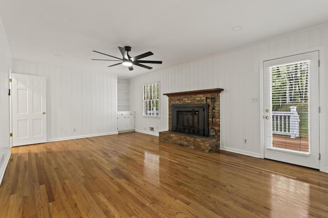 unfurnished living room featuring built in features, plenty of natural light, a fireplace, and hardwood / wood-style floors