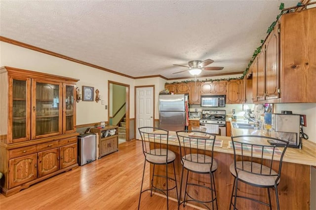 4411 Westerling Ct, Powder Springs, GA 30127 - kitchen featuring stainless steel appliances, a peninsula, brown cabinets, a textured ceiling, and light wood-type flooring