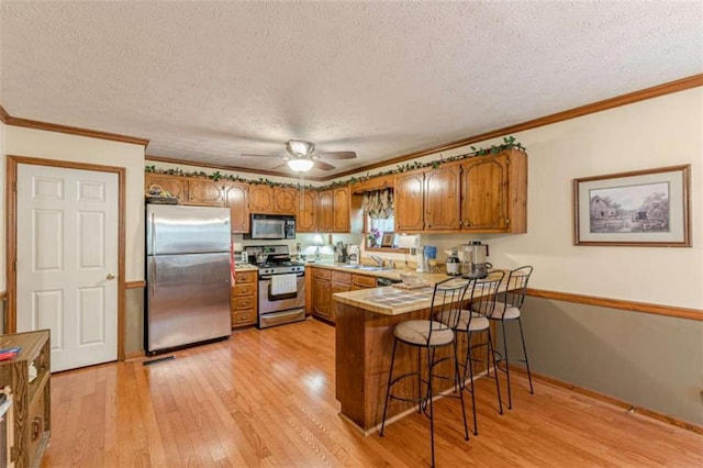 4411 Westerling Ct, Powder Springs, GA 30127 - kitchen featuring appliances with stainless steel finishes, brown cabinets, a peninsula, a textured ceiling, and light wood-type flooring