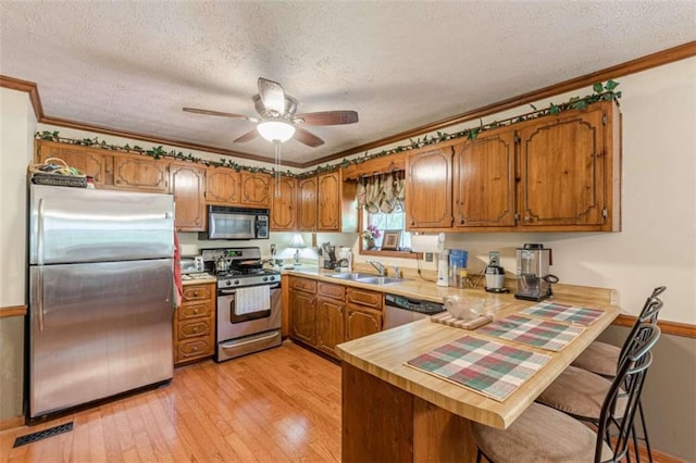 4411 Westerling Ct, Powder Springs, GA 30127 - kitchen featuring appliances with stainless steel finishes, brown cabinetry, a peninsula, crown molding, and a textured ceiling
